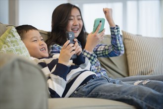 Asian brother and sister using cell phones on sofa