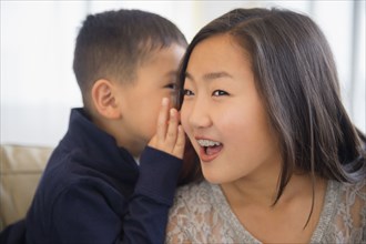 Asian boy whispering in ear of sister