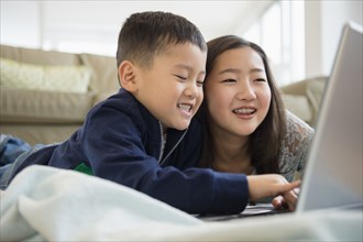 Asian brother and sister using laptop on living room floor