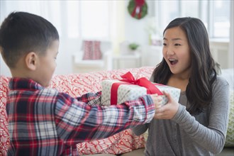 Asian brother giving sister Christmas gift in living room
