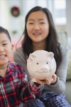 Asian brother and sister holding piggy bank in living room