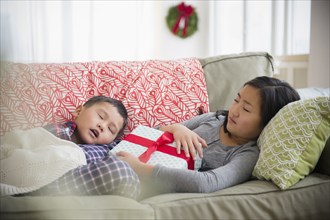 Asian brother and sister napping on sofa with Christmas gift