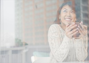 Pacific Islander woman drinking cup of coffee behind window