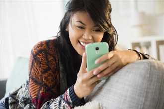 Pacific Islander texting with cell phone on sofa