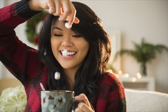 Pacific Islander woman dropping marshmallows into hot chocolate