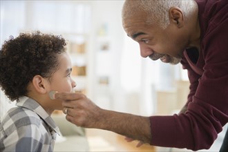 Mixed race grandfather pulling magic coin from ear of grandson
