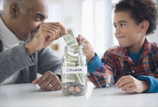 Mixed race grandfather and grandson saving money in college fund jar