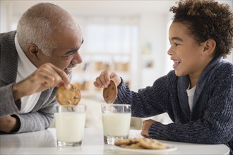 Mixed race grandfather and grandson eating cookies and milk
