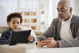 Mixed race grandfather and grandson using cell phone and digital tablet