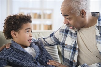 Mixed race grandfather and grandson talking on sofa