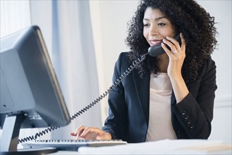 Mixed race businesswoman using telephone and computer in office
