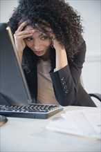 Frustrated mixed race businesswoman working at computer in office