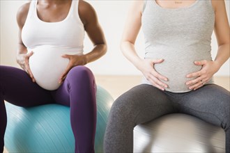Pregnant women holding stomachs sitting on fitness balls