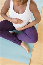 Black pregnant woman sitting on exercise mat holding stomach