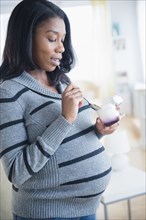Black pregnant woman eating yogurt
