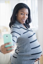 Black pregnant woman taking cell phone selfie