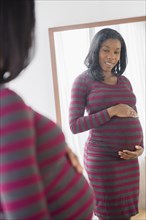 Black pregnant woman admiring her stomach in mirror