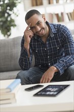 Hispanic man with cell phone and digital tablet in living room