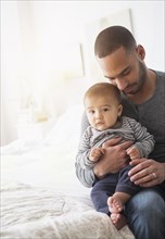 Smiling father holding baby son on bed