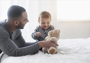 Smiling father playing with baby son on bed