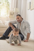 Father watching baby son crawling on floor