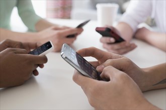 Close up of friends texting on cell phones at table