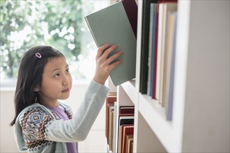 Chinese student selecting book from library bookcase