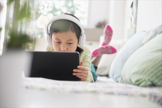 Chinese girl using digital tablet with headphones on bed