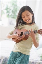 Chinese girl practicing ukulele in bedroom