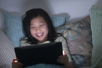 Smiling Chinese girl watching digital tablet in bed