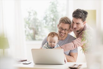 Caucasian gay fathers and baby using laptop