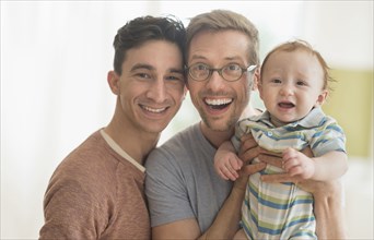 Smiling Caucasian gay fathers holding baby