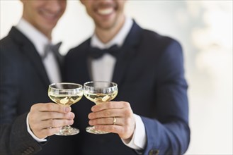 Caucasian gay grooms toasting with champagne at wedding