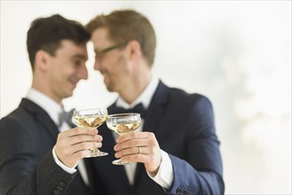 Caucasian gay grooms toasting with champagne at wedding
