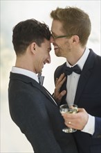 Caucasian gay grooms drinking champagne at wedding