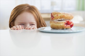 Caucasian girl peeking at donuts on table