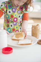 Caucasian girl spreading peanut butter on bread