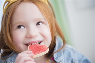 Caucasian girl eating heart-shape cookie