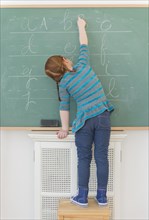 Caucasian girl writing on chalkboard in classroom