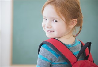 Caucasian girl wearing backpack in classroom