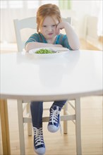 Caucasian girl pouting at plate of vegetables