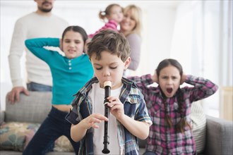 Caucasian family covering ears with boy playing recorder