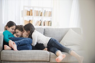 Caucasian brother and sisters whispering on sofa