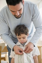 Caucasian father buttoning shirt for son