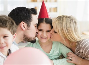 Caucasian parents kissing daughter at birthday party