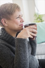 Caucasian woman drinking cup of coffee on sofa