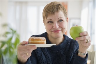 Caucasian woman choosing between donut and apple