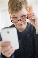 Caucasian woman peering over eyeglasses at cell phone
