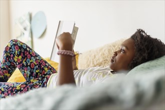 Black girl reading book on bed