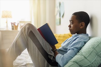 Black boy reading book on bed